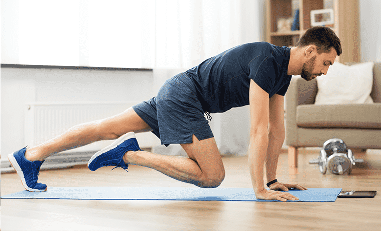 A man works out on a yoga mat at home while wearing a fitness tracker.