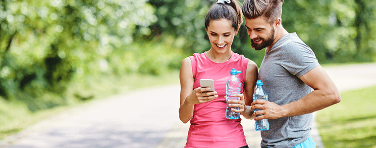 A man and woman take a break on their run and look at an app on their smartphone.