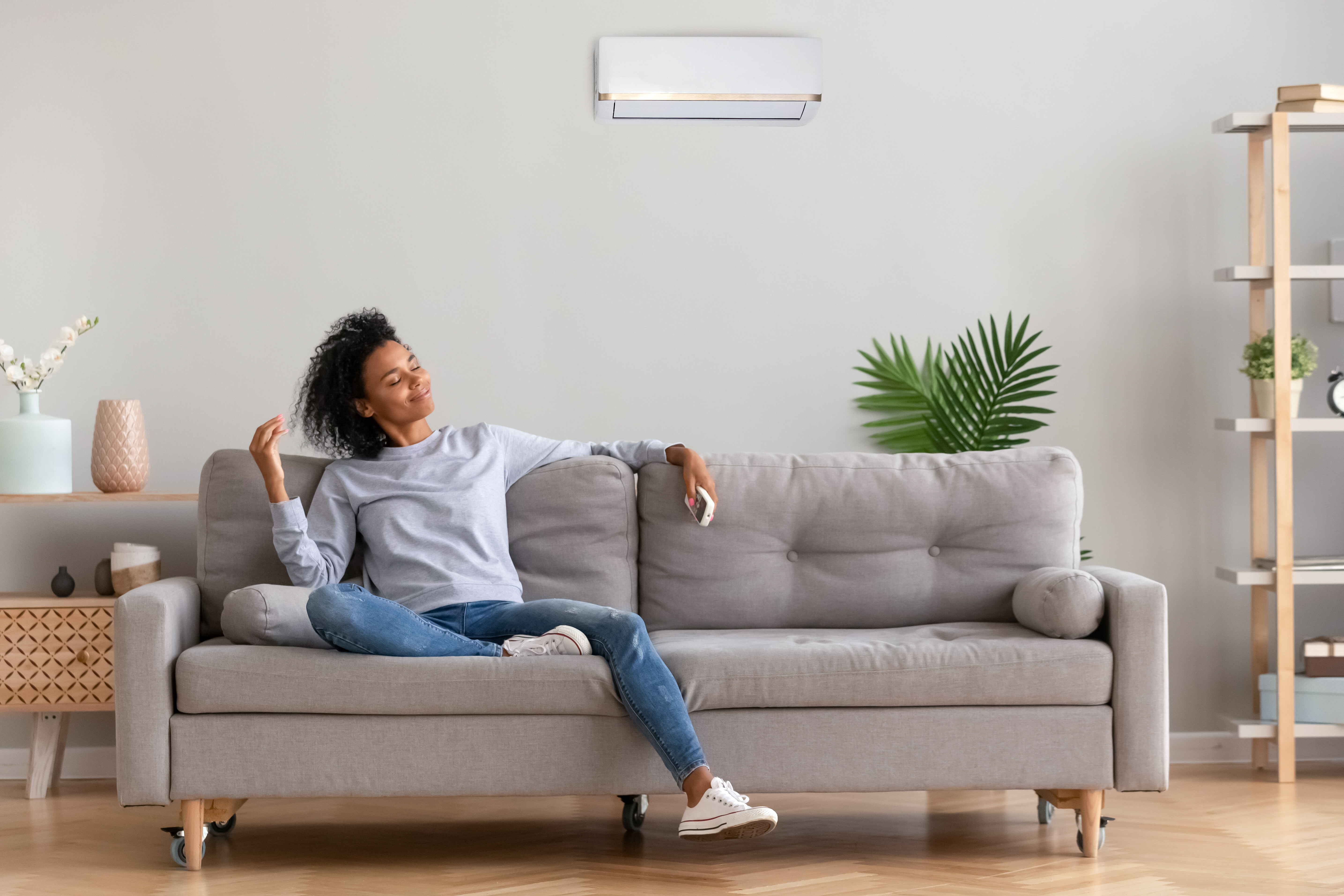 A woman relaxes in her living room while her split system air conditioner keeps the room cool.
