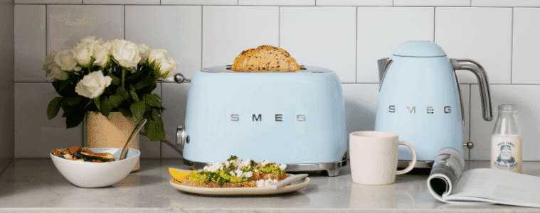 Smeg retro toaster and kettle in sky blue on a white benchtop with an assortment of food around them.