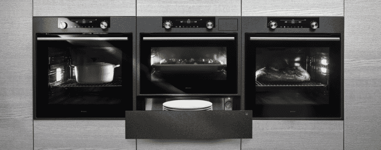 Three black built-in wall ovens on grey cabinets. 