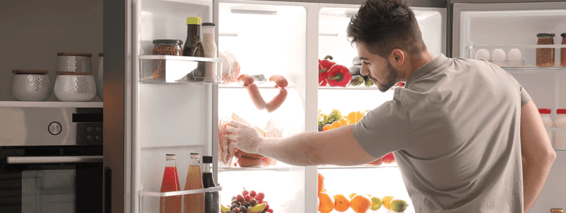A man grabs food out of his French door fridge.