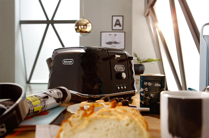 Modern black Delonghi toaster on a benchtop with bread and pastries