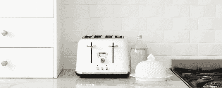 A kettle sits on a bench in front of a white tiled splashback.