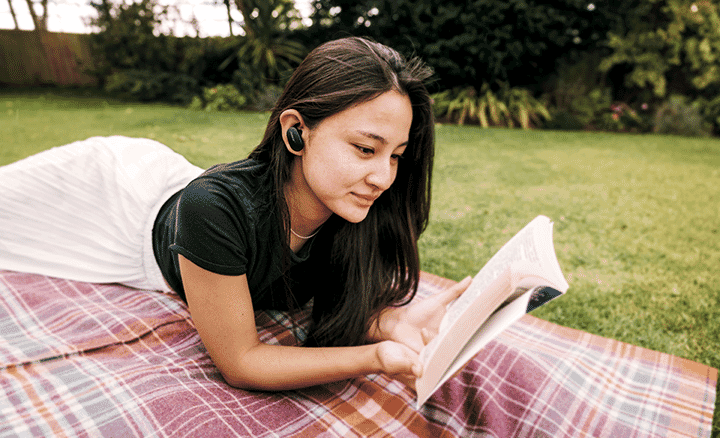 Woman relaxing in a park whilst reading and using her new Noise Cancelling Headphones.