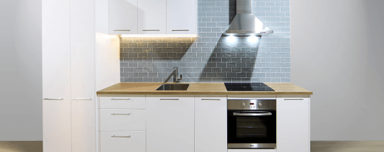 A white flat pack kitchen with blue splashback tile and a timber countertop.