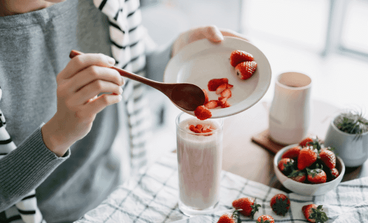 A young woman makes a fresh and healthy strawberry smoothie for breakfast, using a blender on her kitchen bench
