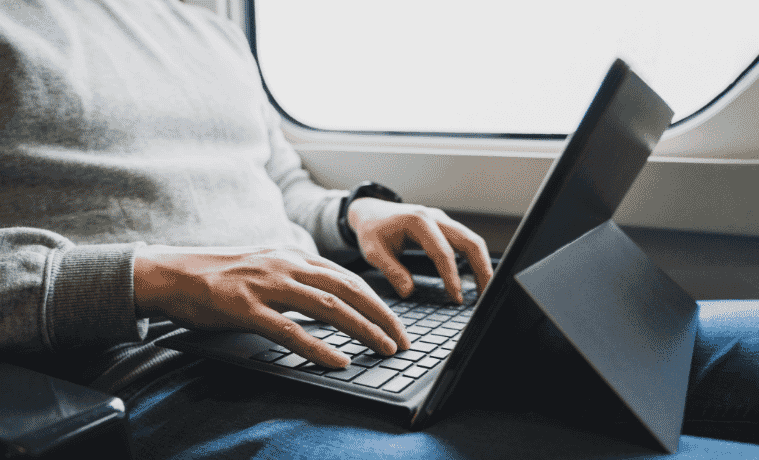 A man types on a laptop while riding the train.