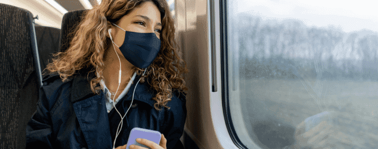 A woman, wearing a mask, sits on a bus.