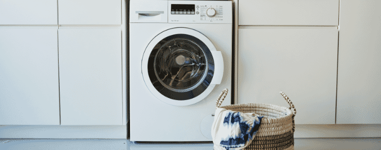 A white washing machine in a white laundry with a basket of washing in front of it.