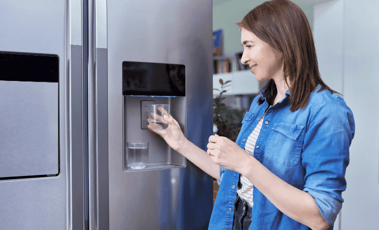 Woman fills a glass of water from the dispenser on her fridge