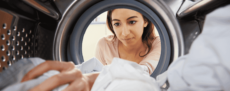 A woman reaches inside her dryer to remove some freshly dried clothes.