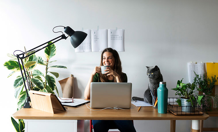 Smiling businesswoman with cat on desk having a coffee in her home office