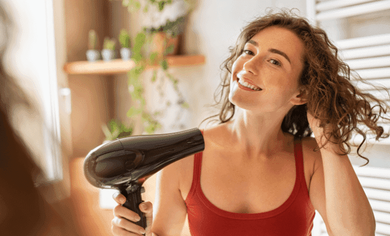 A woman dries her hair with a hair dryer while looking in the mirror.