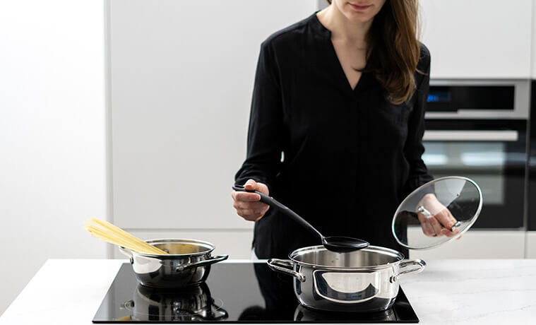 Woman cooks spaghetti on the cooktop in a modern kitchen