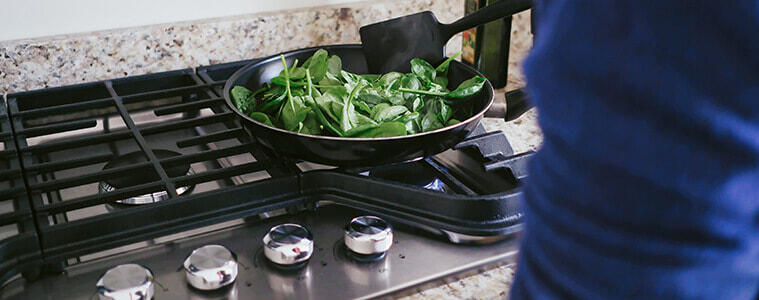 Close-up of a woman sautéing spinach on a cooktop.