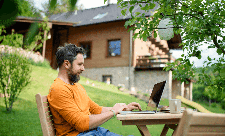 A man works on his laptop while sitting outside.