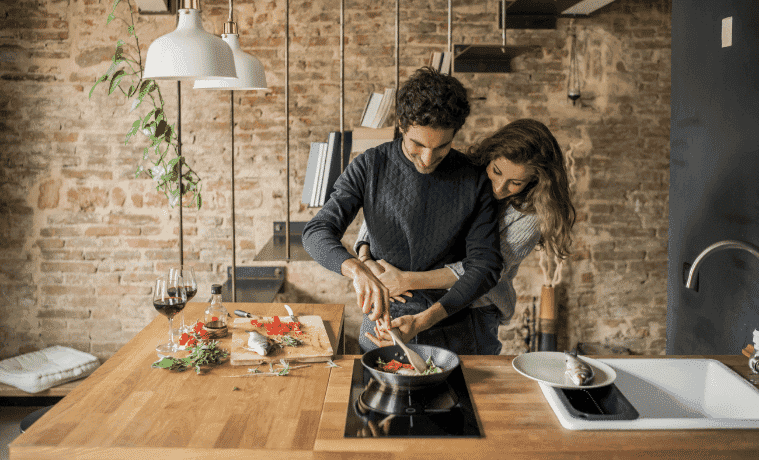 A loving couple, arms wrapped around each other, cook dinner together in their kitchen