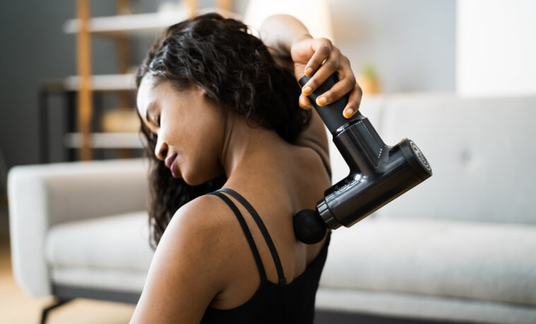 Woman in activewear using a massage gun on her back