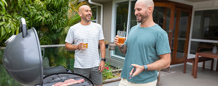 Two men barbeque together outside.