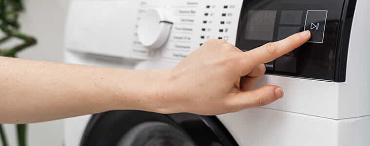A person presses the start button on their washing machine.