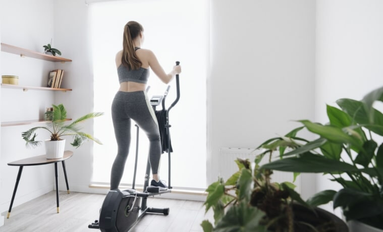 A woman performs a workout on an elliptical trainer at home.