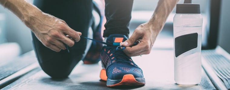 A man bends to tie his shoelaces before hitting the treadmill in his home gym.