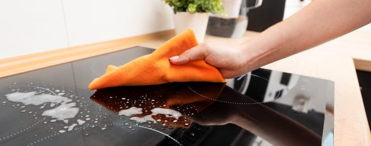 A woman uses a cloth to wipe clean her induction cooktop.