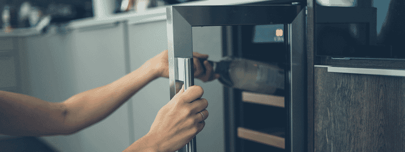 Woman opening her wine fridge in the kitchen to put away a bottle of wine.