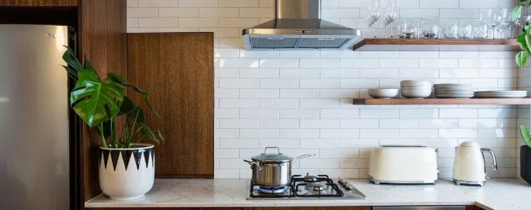 A chrome canopy rangehood in a white and warm timber kitchen.