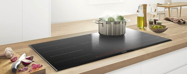 A built-in cooktop on a blonde timber butchers block countertop.