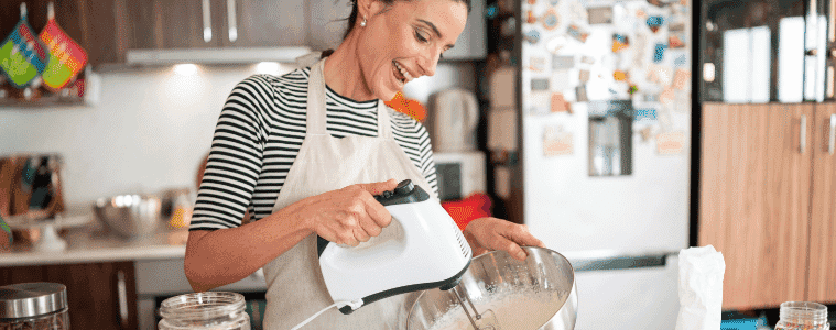Woman in apron using kitchen mixer while smiling