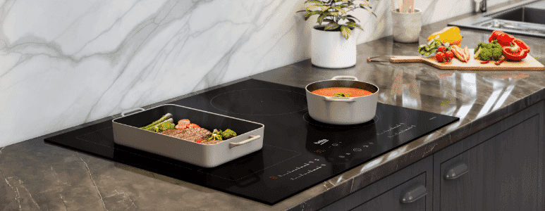 Induction cooktop with a pot that has soup in it and another dish that has some meat and vegetables.  