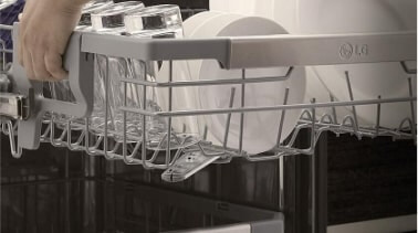 A person uses the handles on the side of the top rack to lower the basket in their LG QuadWash dishwasher.