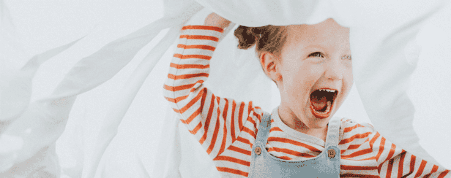 A little girl plays with freshly laundered bed sheets.