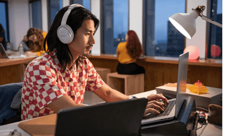 Man happily working on his laptop at a desk whilst using his over ear Bose Noise Cancelling Headphones