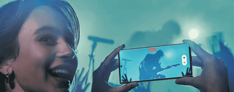 Smiling woman taking a video at a concert using her new Samsung Galaxy S23 mobile phone.