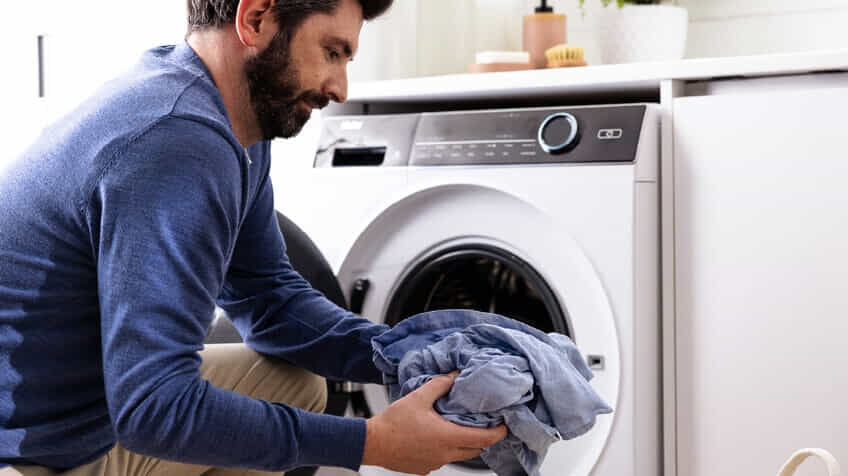 A man holds freshly dried laundry that he has pulled out of his Haier dryer.