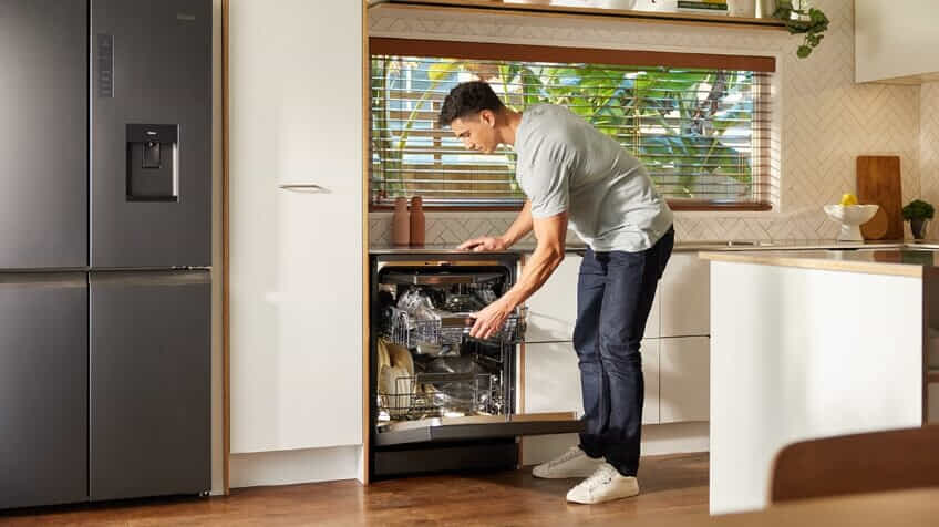 A man unloads his clean dishware and cutlery from his Haier dishwasher.