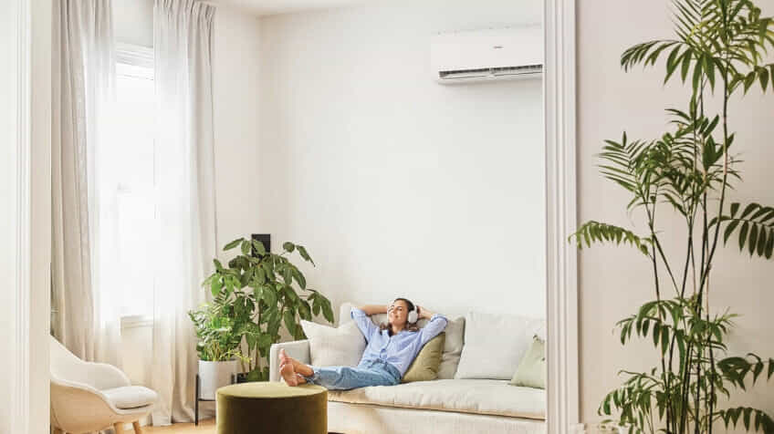A woman relaxes in her living room while her Haier air conditioner heats the room.