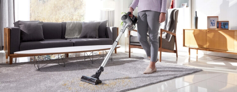 Woman using her LG A9K-Evolve across tiles and a rug for a seamless clean.
