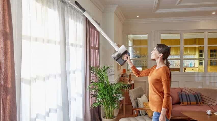 Woman using her LG CordZero vacuum to clean above her window sill.