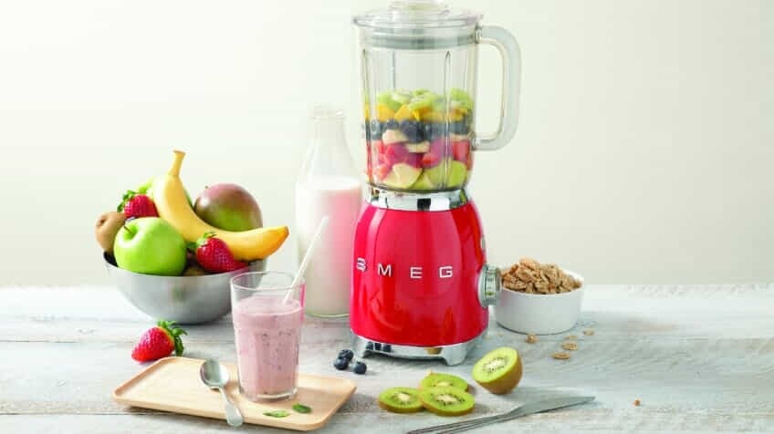 A red Smeg retro blender filled with fruit for a smoothie.