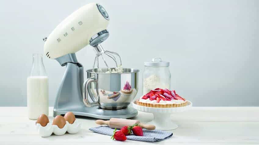 A cream coloured Smeg stand mixer, mixes cream for a strawberry pie.