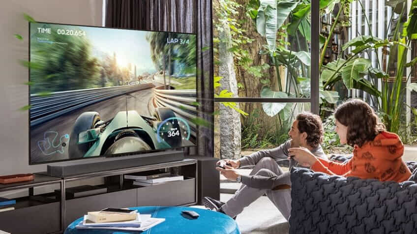 Two people playing a video game sitting in front of a Samsung TV and soundbar.