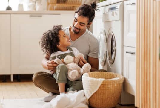 a dad and his son sitting in front of their washer waiting for their clothes