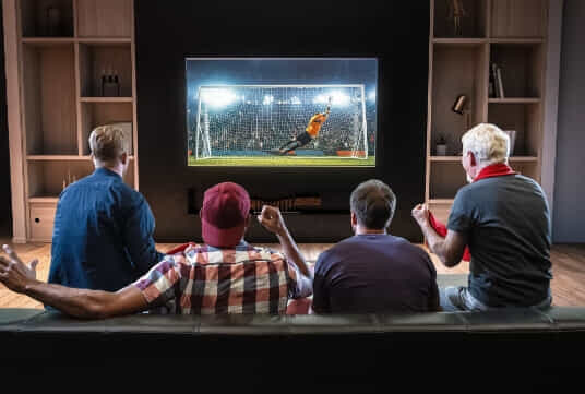 Generations of men sitting down to watch a soccer match. 