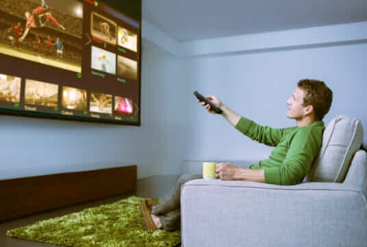 Man kicking back to enjoy watching some sport. 