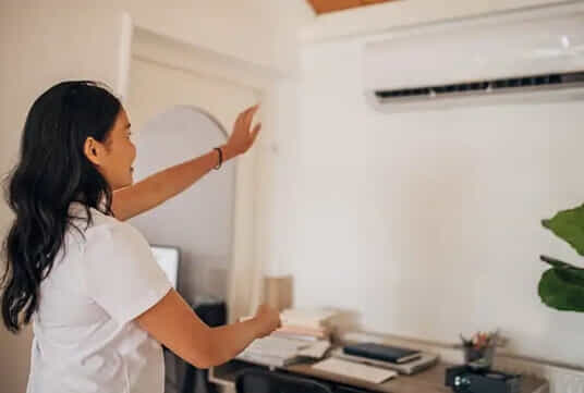 A woman feels the heat coming out of her split system air conditioner.