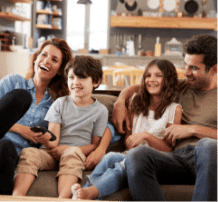 Family of 4 sitting on the couch watching TV together.